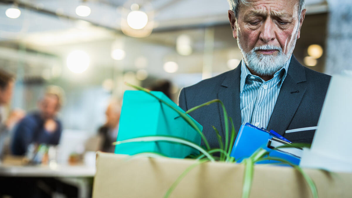 Man looking disappointed while holding a box full of desk supplies.