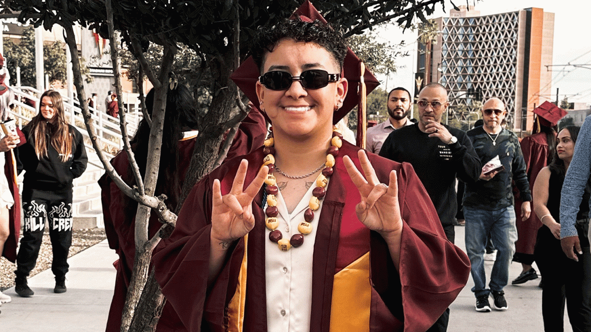 ASU Local student Olivia Covarrubias poses in graduation cap and gown while holding up two pitchfork hand gestures