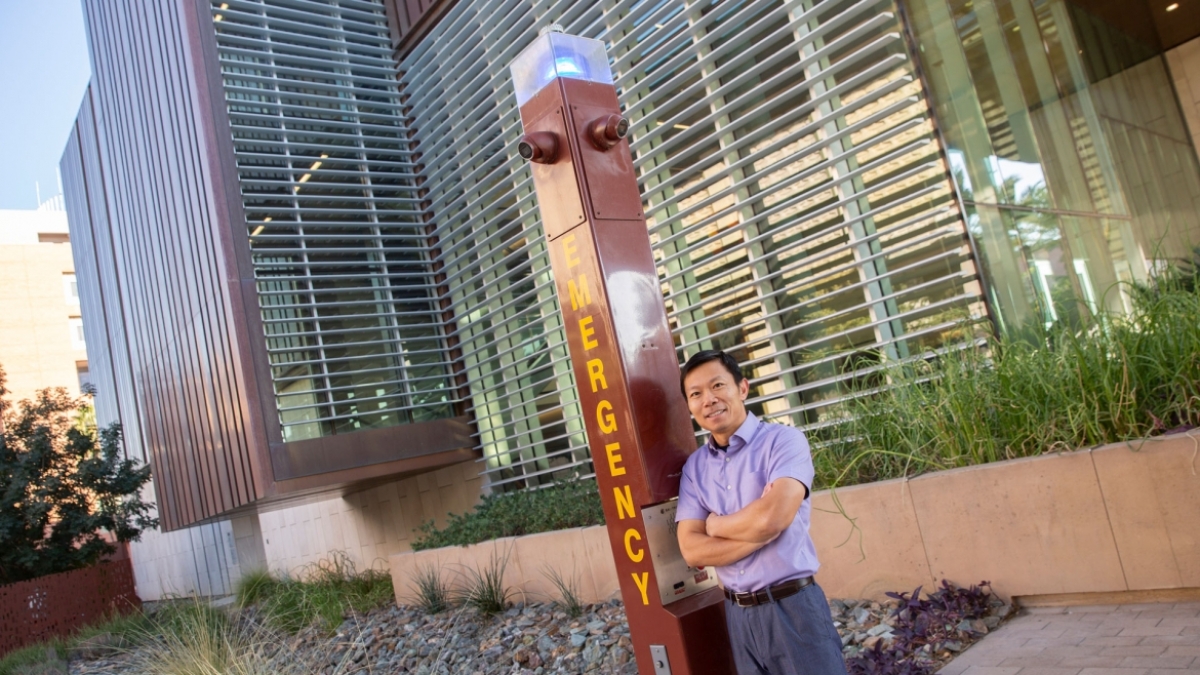 Man standing next to an emergency call station on a university campus.