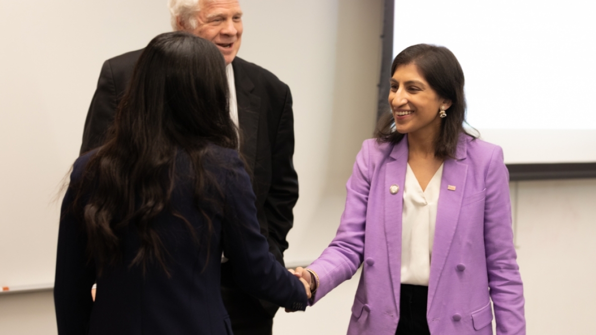 A brunette woman in a purple blazer shakes hands with a student.