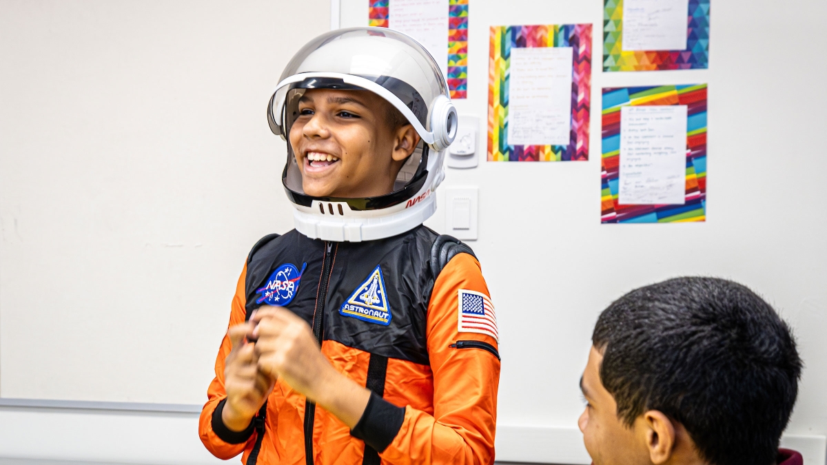 A boy wearing an astronaut costume smiles wide at someone off camera