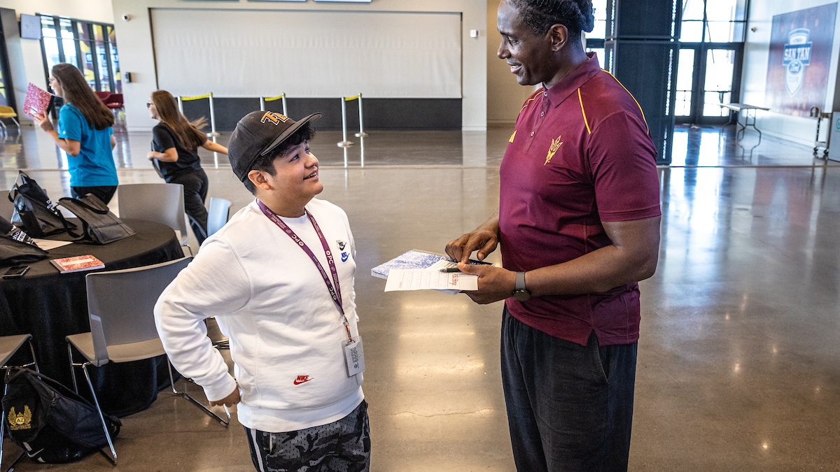 Man wearing an ASU shirt speaking to a young student.