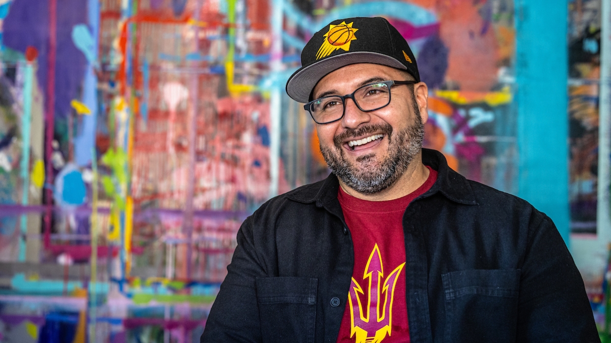 Miguel Godoy smiling in front of a colorful mural.