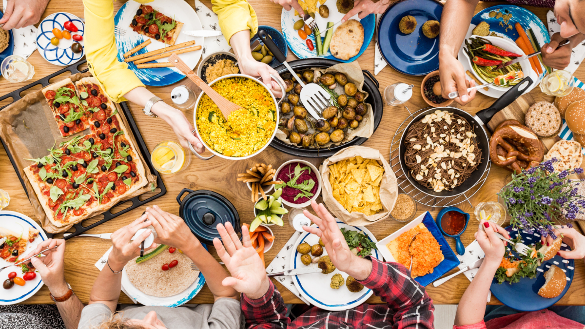 Bird's eye view of a food-filled table with hands passing food around.