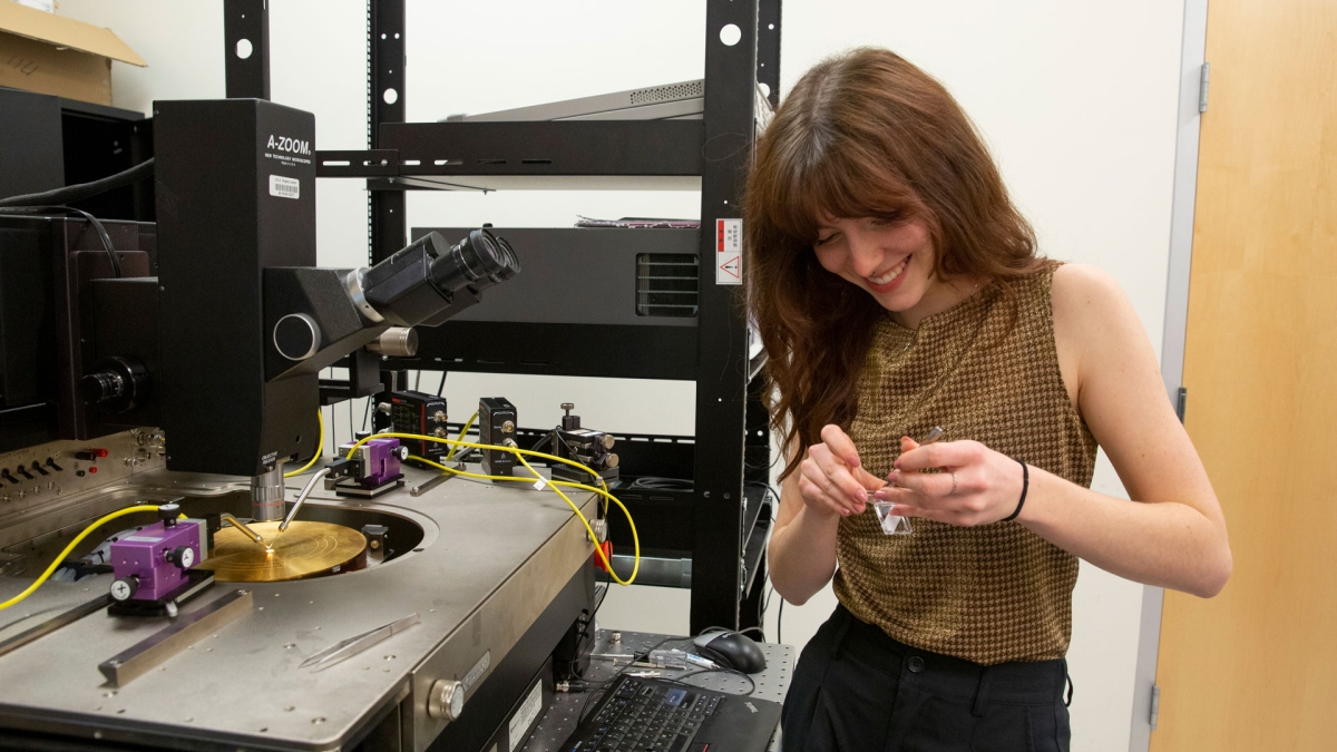 A student adjusts a research sample while standing next to lab equipment. 