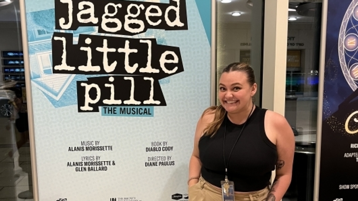Woman standing next to Jagged Little Pill poster
