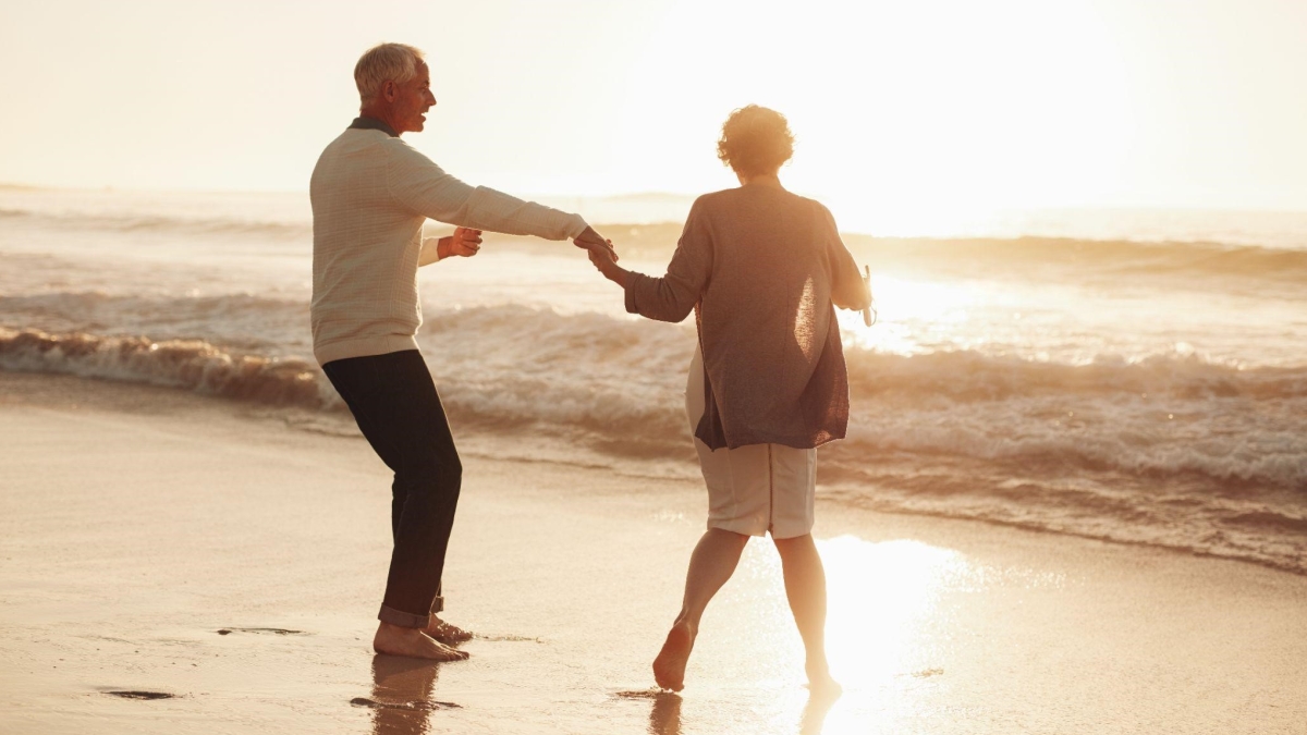 Two older adults holding hands while dancing on a beach at sunset