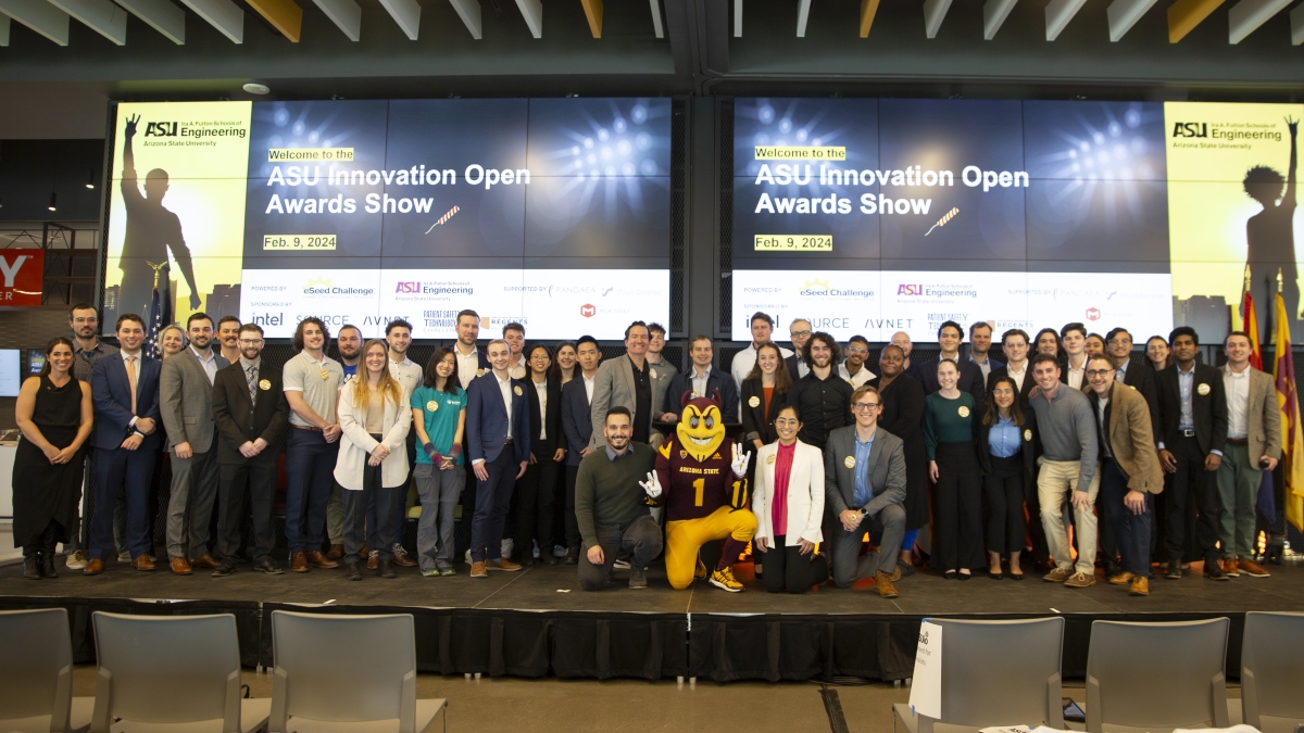 Group of students pose for a photo onstage with screens reading "ASU Innovation Open Awards Show" in the background and ASU mascot Sparky in the middle.