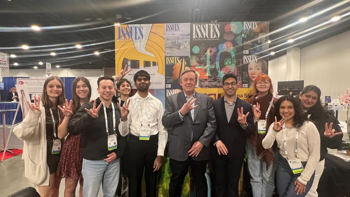 A group of students and Michael Crow holding up the "forks up" symbol at AAAS.
