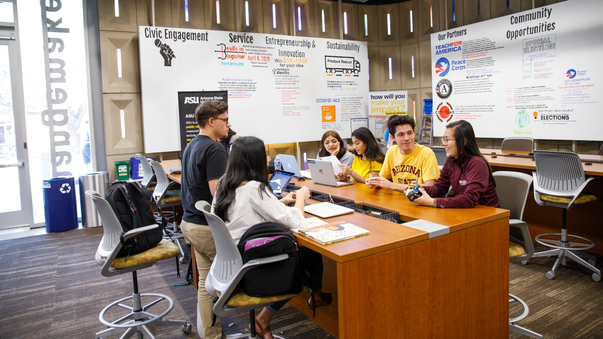 Six members of the ASU community sit around a desk, smiling and sharing conversation. 