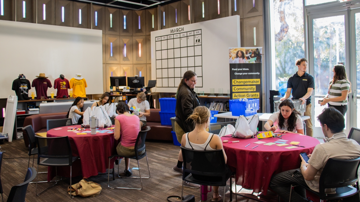 People seated at multiple tables inside a store with ASU merch and colors on display.