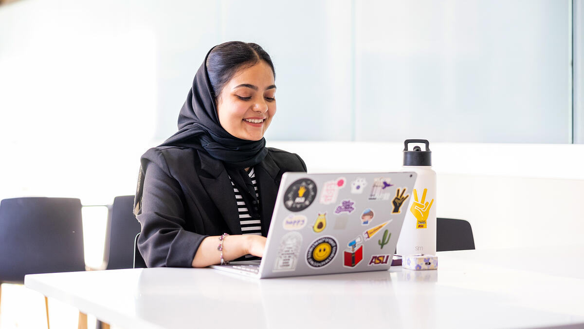 A woman wearing a hijab works on a laptop at a white table.