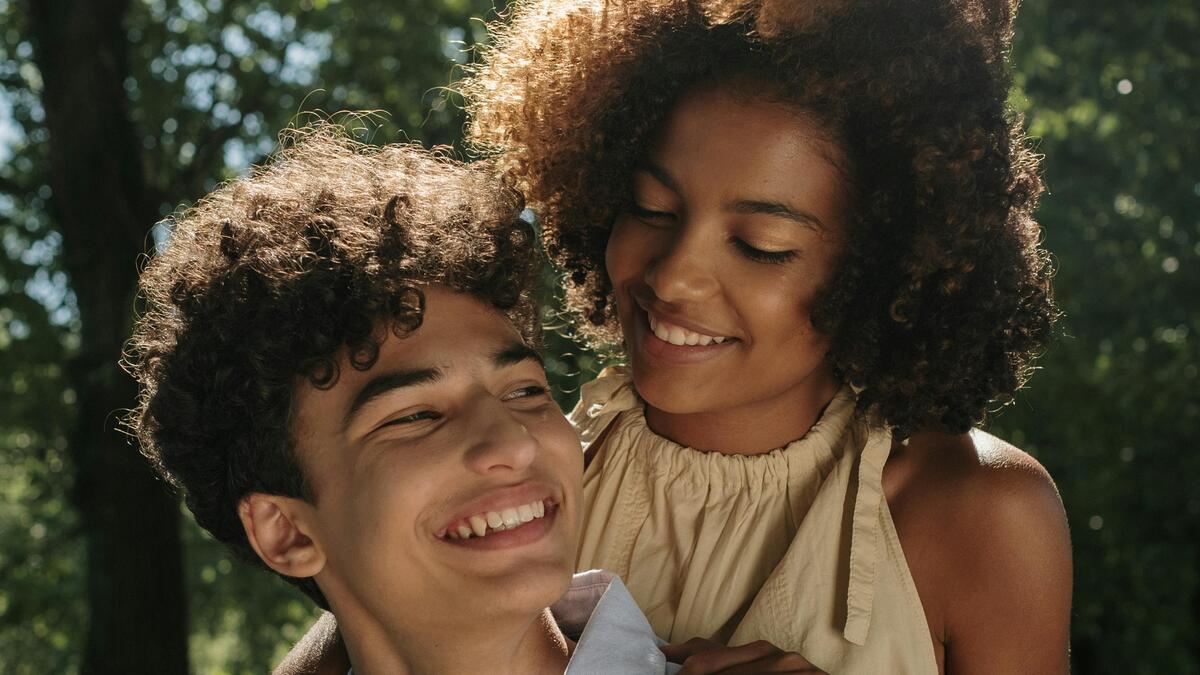 Two teenagers hug and smile at each other.