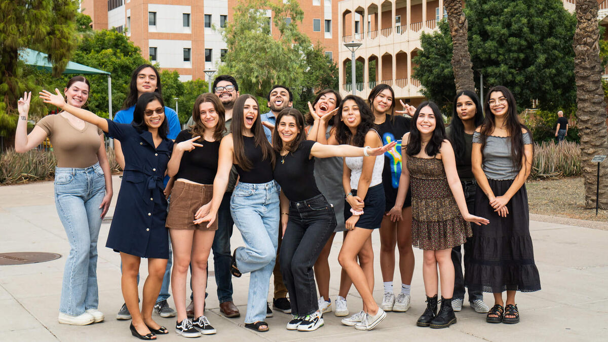 A group of students pose with a professor on a college campus.