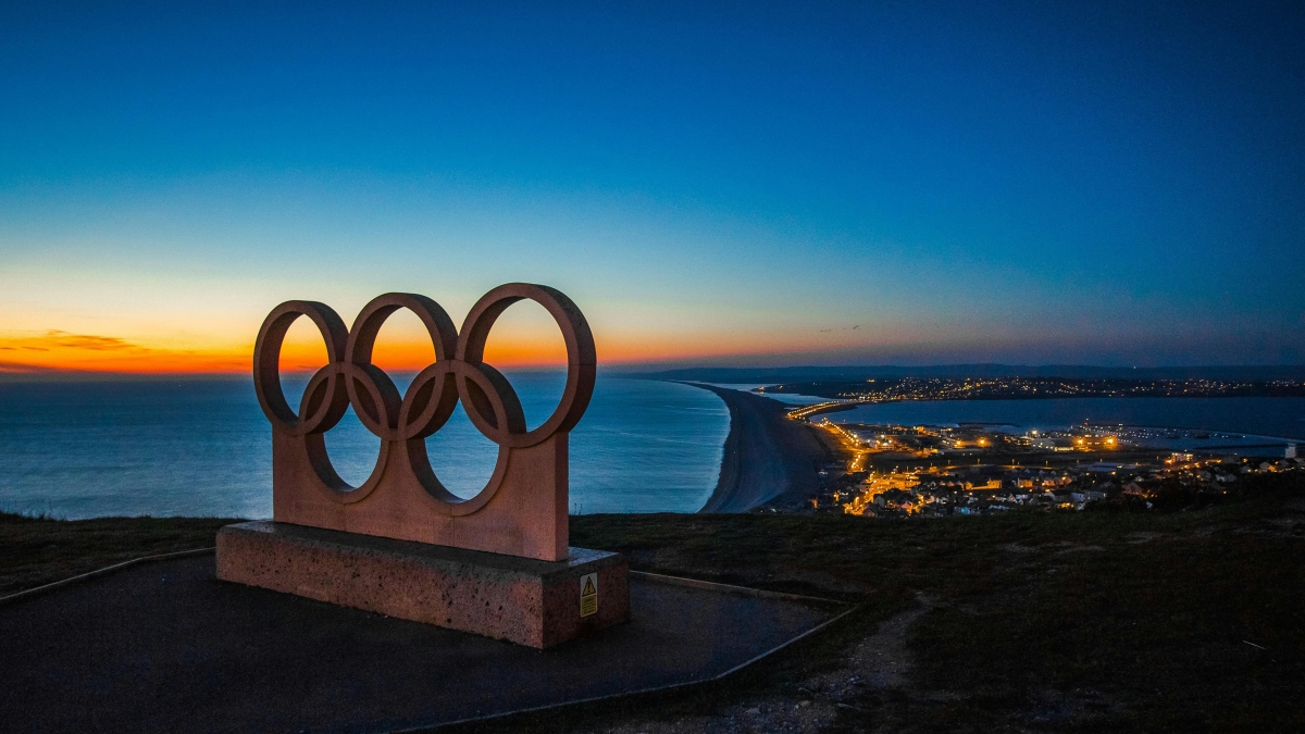 Olympic rings with a coastal city lit at night in the background.
