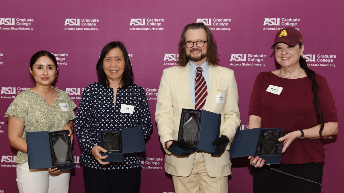 Four people stand in a line smiling holding awards