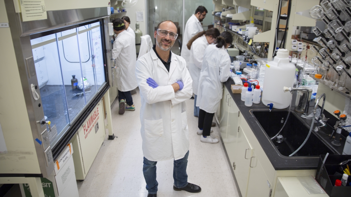 Sergi Garcia-Segura standing looking at the camera smiling with arms folded in his lab while others work in the lab behind him
