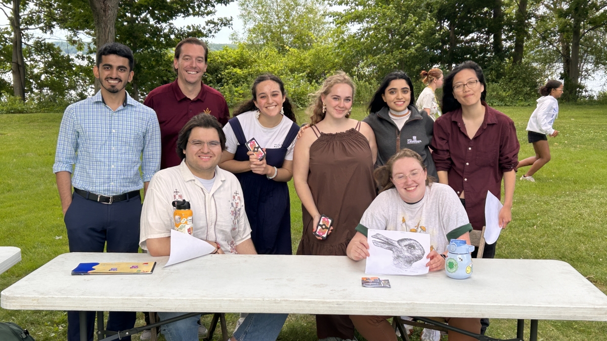 Students smile at the camera while sitting at a white picnic table outside.