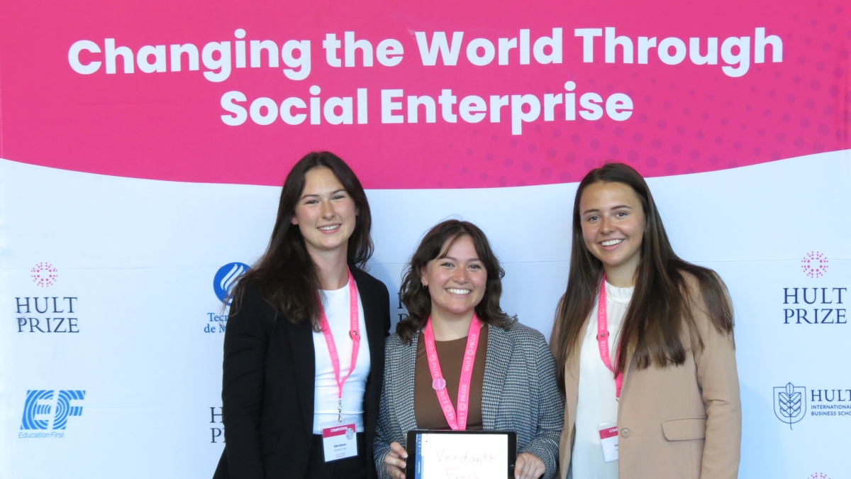 Three women pose holding an award with a banner behind them reading "Changing the World Through Social Enterprise"