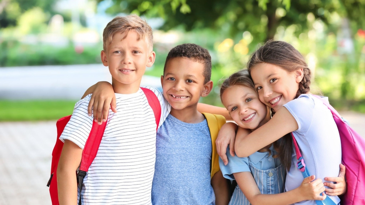 Four kids with backpacks on and arms around each other 