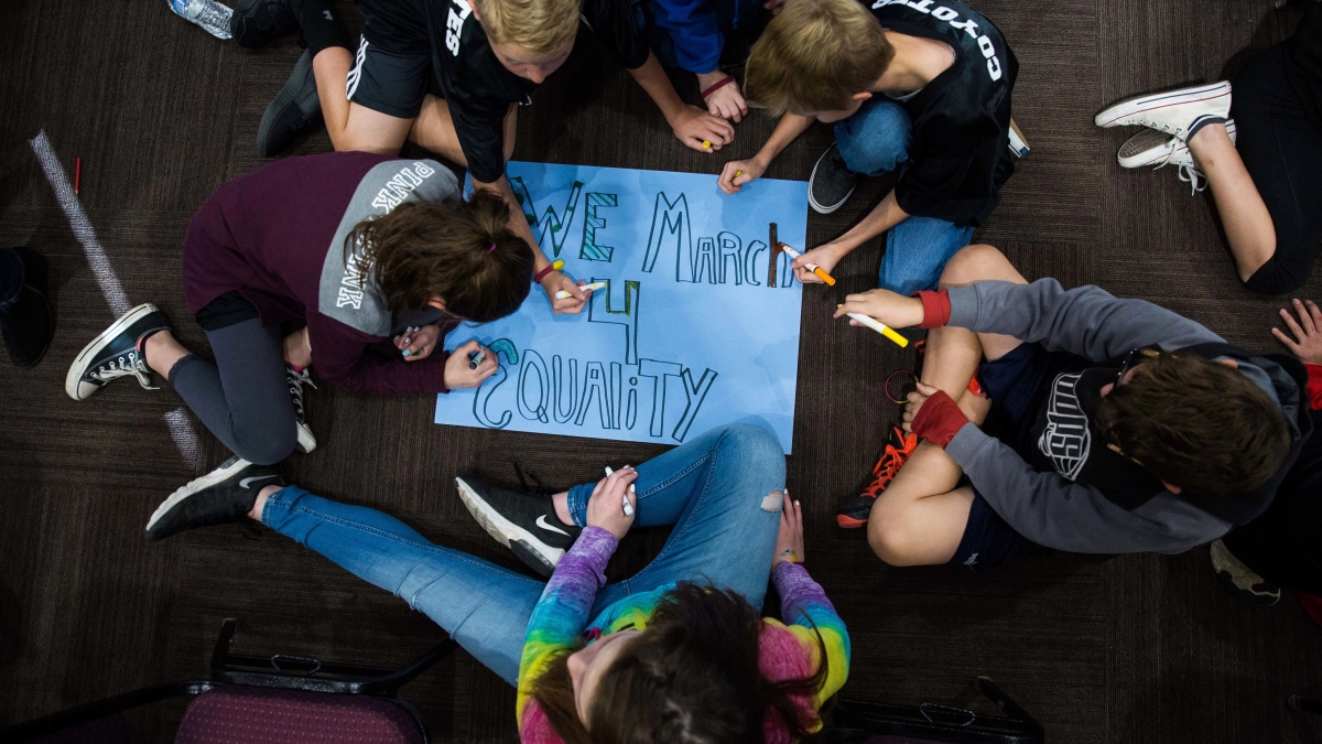 Students drawing on a sign that says "We March 4 Equality"