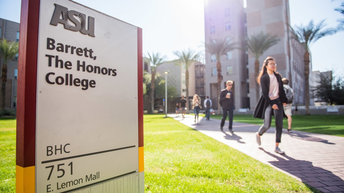 Sign that reads "Barrett, The Honors College" on a campus with students walking around it.