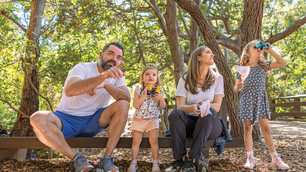 A family sitting on a bench in a wooded area looking at nature