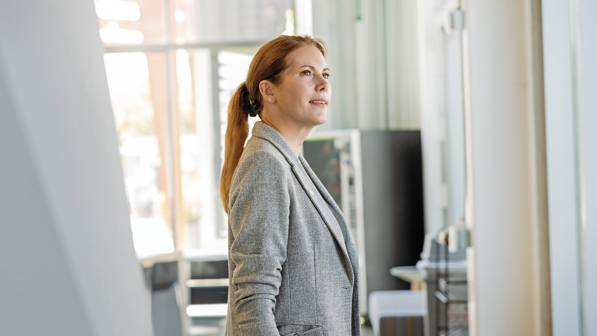 Portrait of a woman with reddish brown hair wearing a gray blazer in an office break room