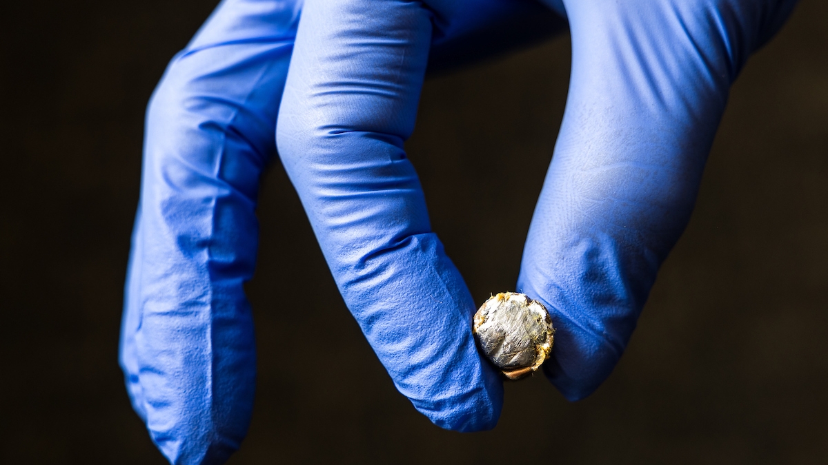 Two gloved fingers holding a bullet