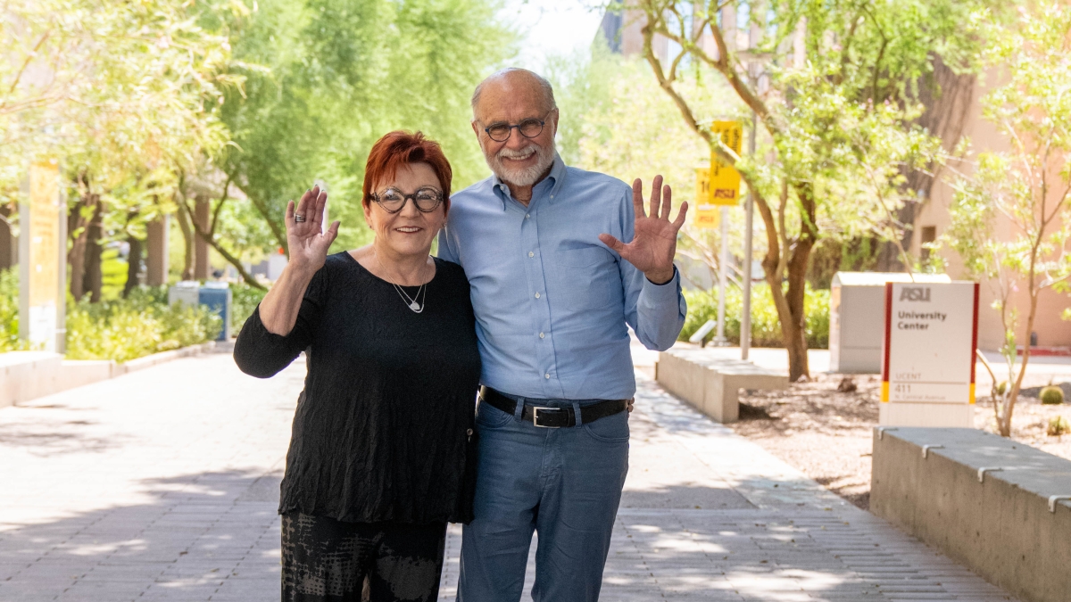 A woman and a man pose for a photo while waving at the camera