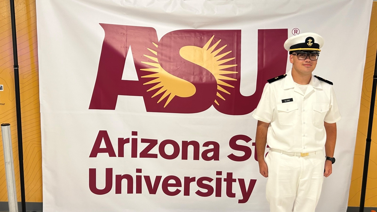 Man wearing Navy dress whites standing in front of a sign that says "Arizona State University."