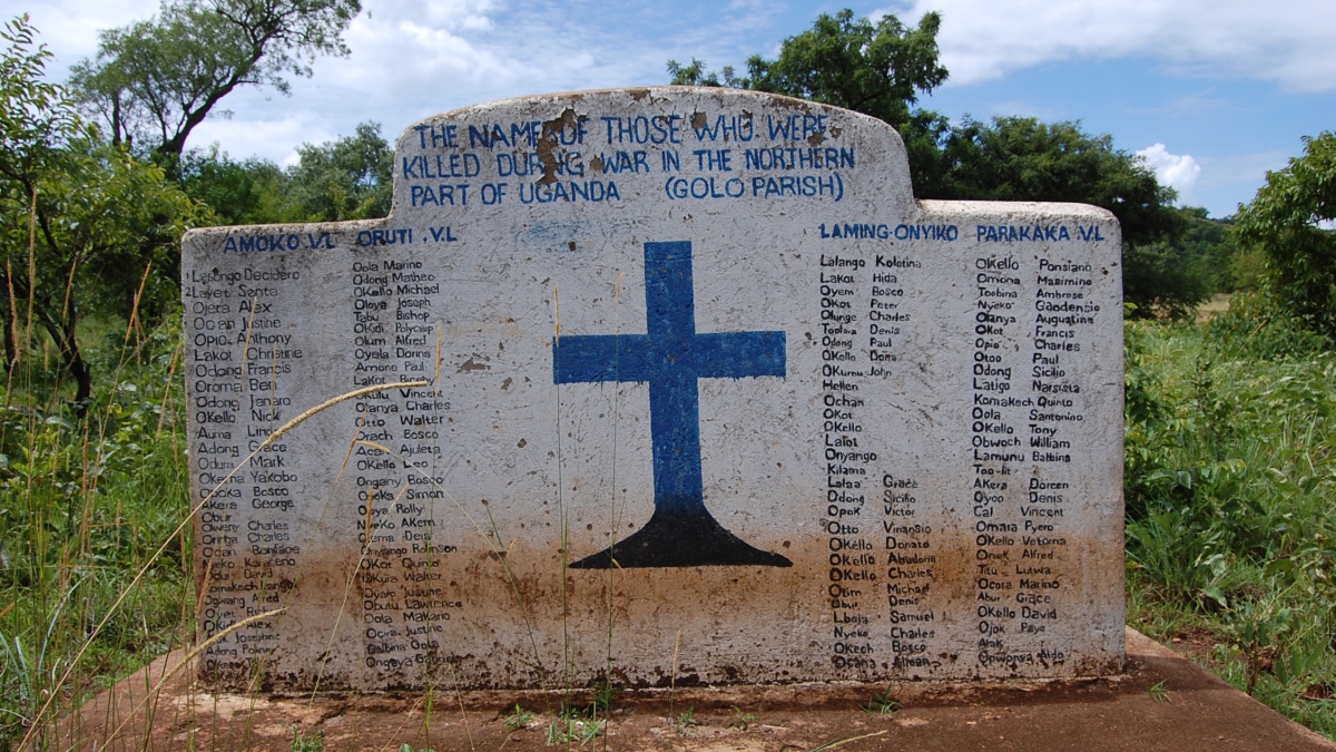 Concrete memorial at an outdoor burial site in Uganda with a blue cross and writing on it