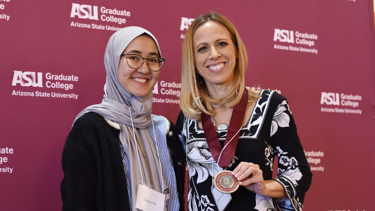 Two women smile at the camera as one holds a medal.