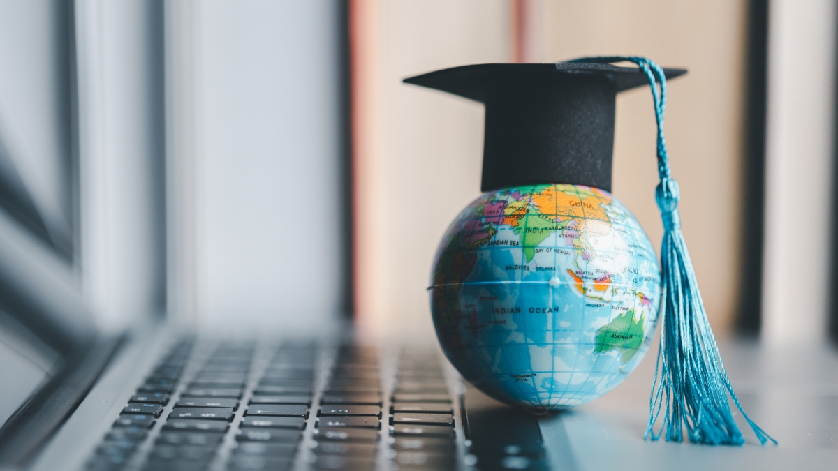 A tiny globe wearing a tiny graduation cap sits on a laptop keyboard