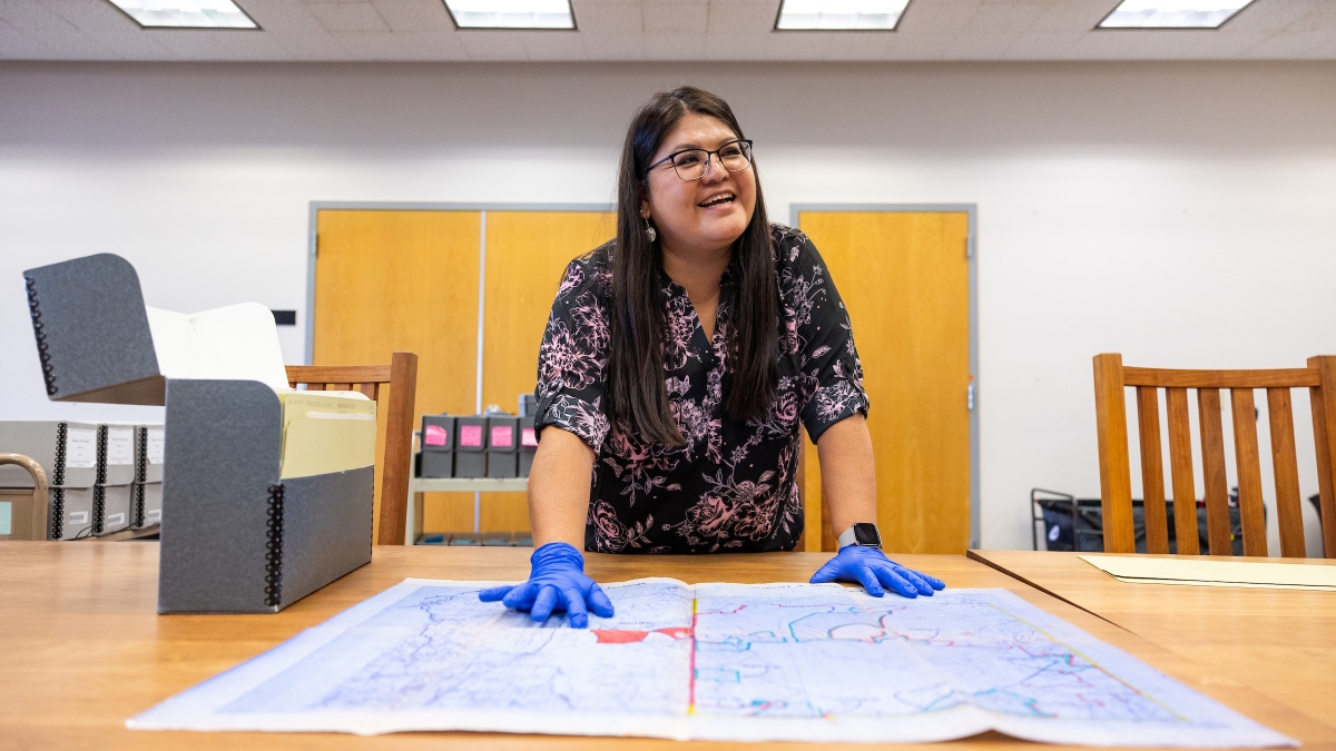 Woman wearing blue gloves leaning over a table with a map on it.