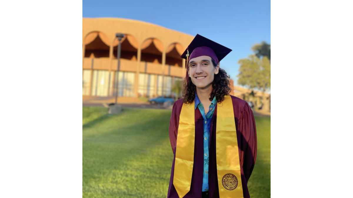 Zachary Cooper standing in graduation regalia in front of Gammage Auditorium on the Tempe campus