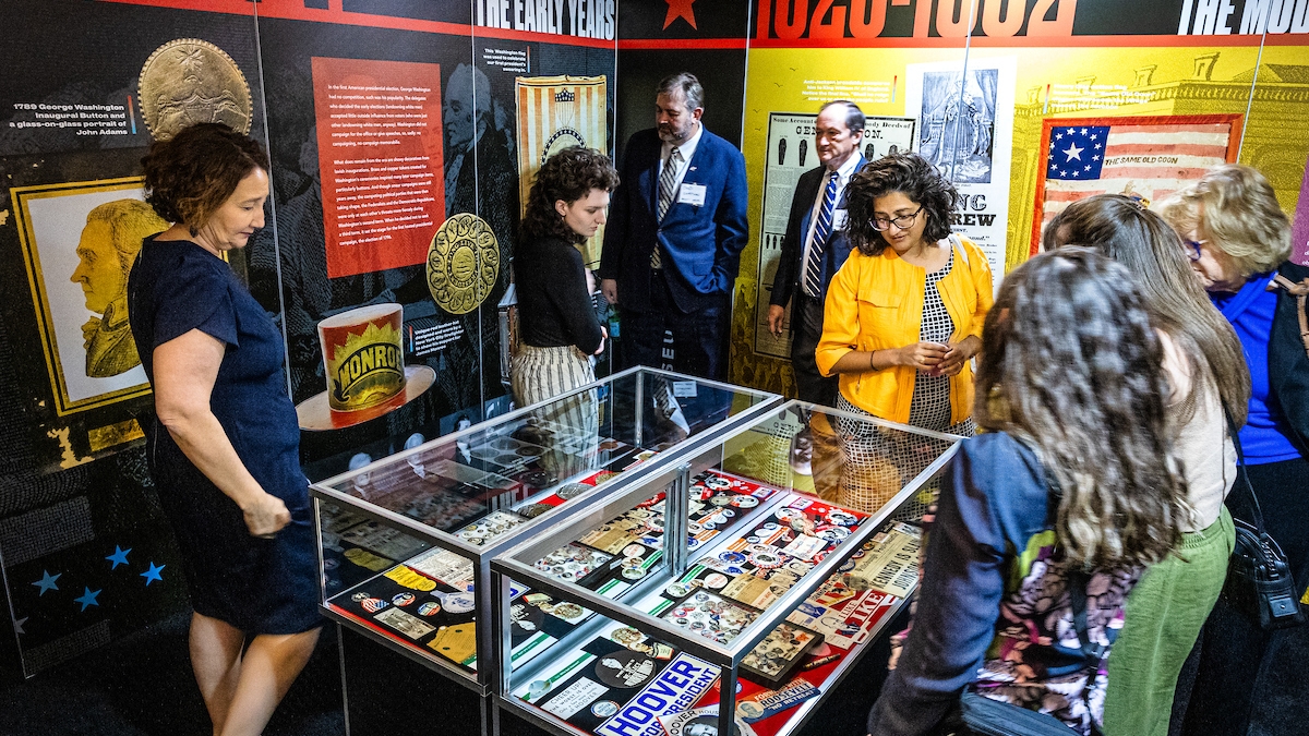 People gather around display of campaign memorabilia at the opening reception for "We the People..." exhibit