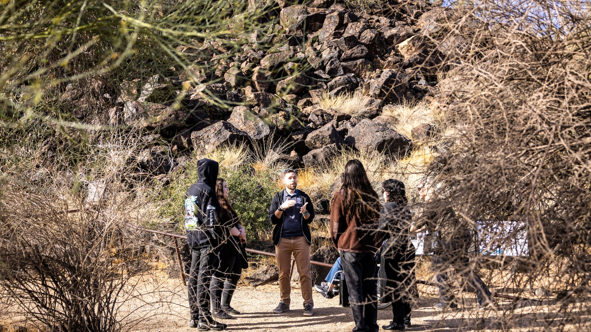 A guide leading a group of people on a tour of a outdoor petroglyph preserve