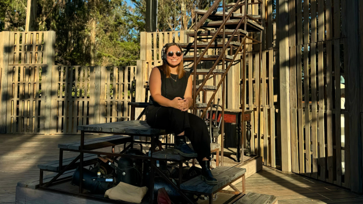 Woman sits on a chair behind a stage in an outdoor theater.