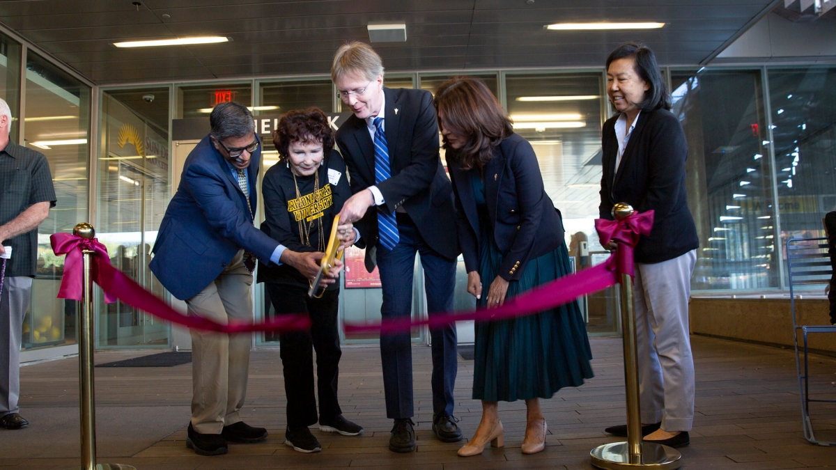 Group of people use large scissors to cut a ribbon outside of a building.