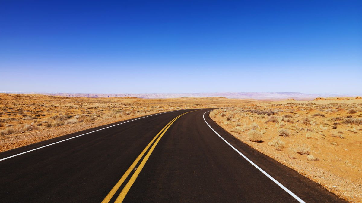 A two lane highway is visible with wide stretches of desert on either side. Blue skies and some mountains are in the distances