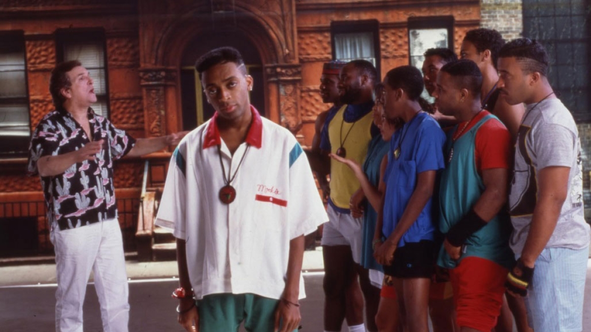 Man standing on an urban street faces the camera while behind him, another man faces a group of other men.