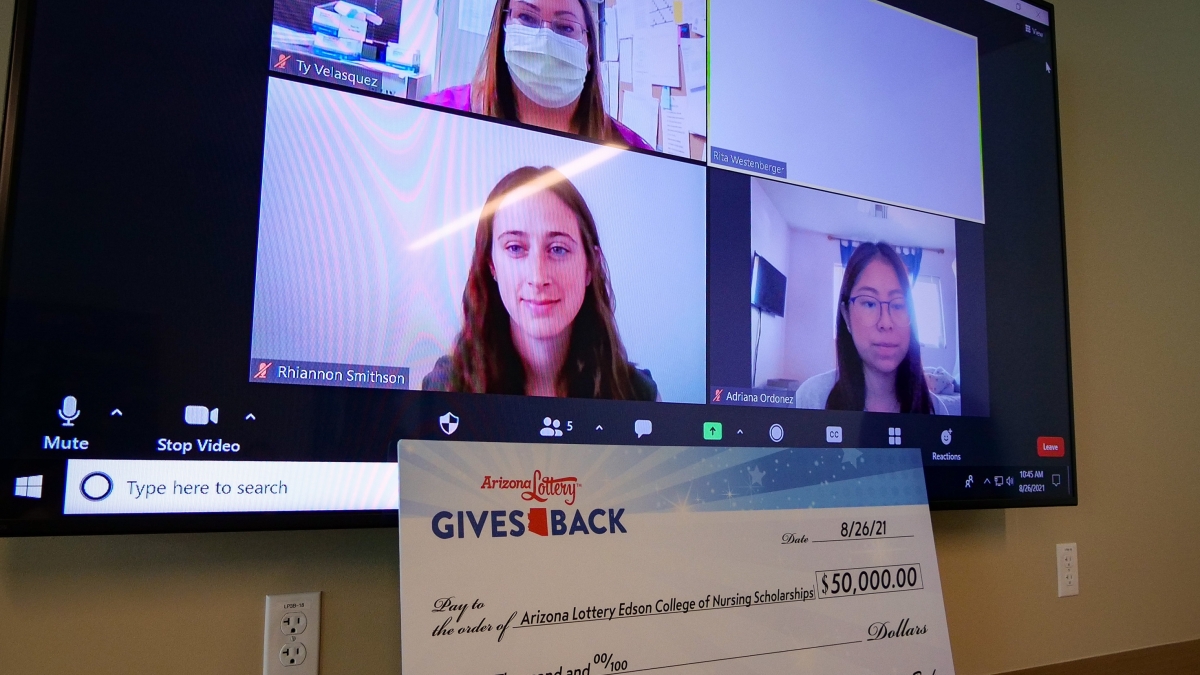 Three Edson College students are on a big screen Zooming into a scholarship awards presentation. Below the screen is a large check