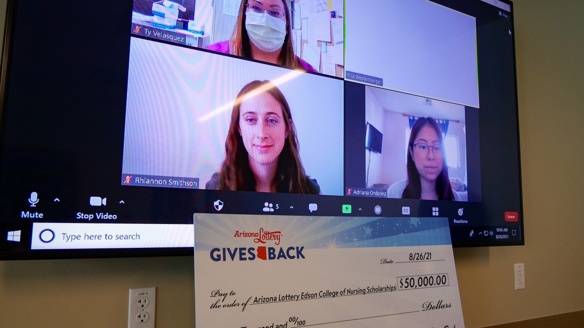 Three Edson College students are on a big screen Zooming into a scholarship awards presentation. Below the screen is a large check