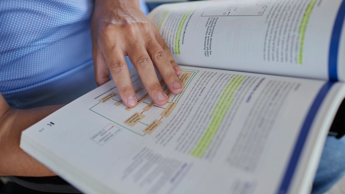 A hand holding a textbook open to a page with highlighted text.