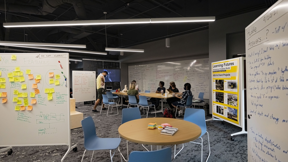 People sit at a round table in a room with whiteboard.