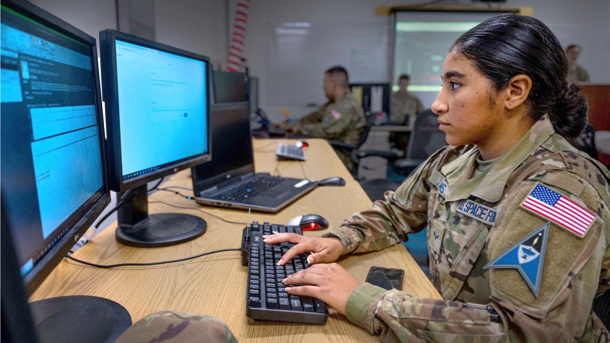 Woman wearing military fatigues seated at a computer typing.