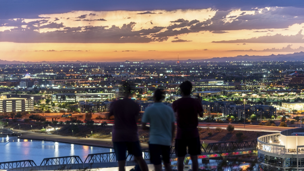 Three people looking out at Tempe skyline at dusk