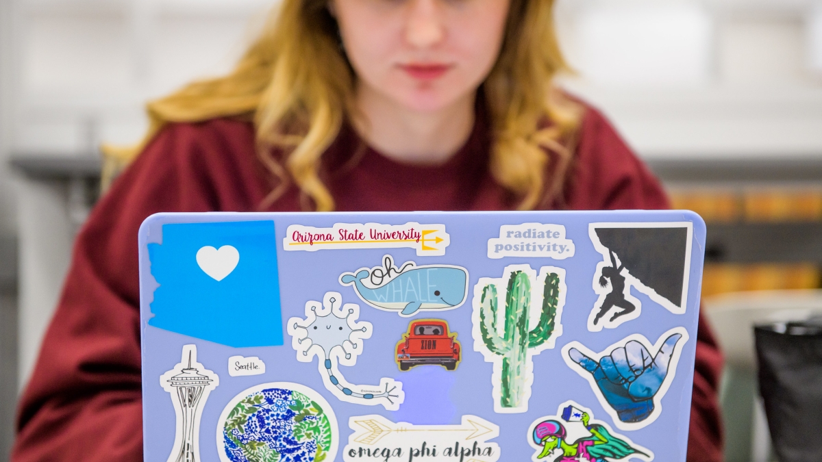 A female student works on a laptop covered in ASU stickers