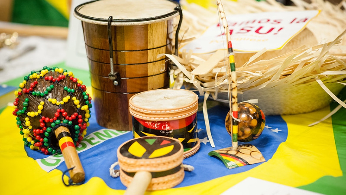 Culturally specific percussive musical instruments cover a table. They are light tan and medium brown in color with red, green and yellow accents.